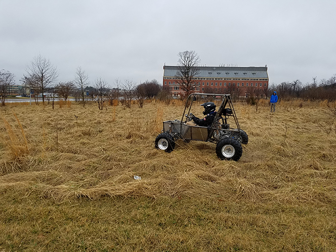Baja vehicle being test driven on bumpy field near Exploration Hall at GW's VSTC campus