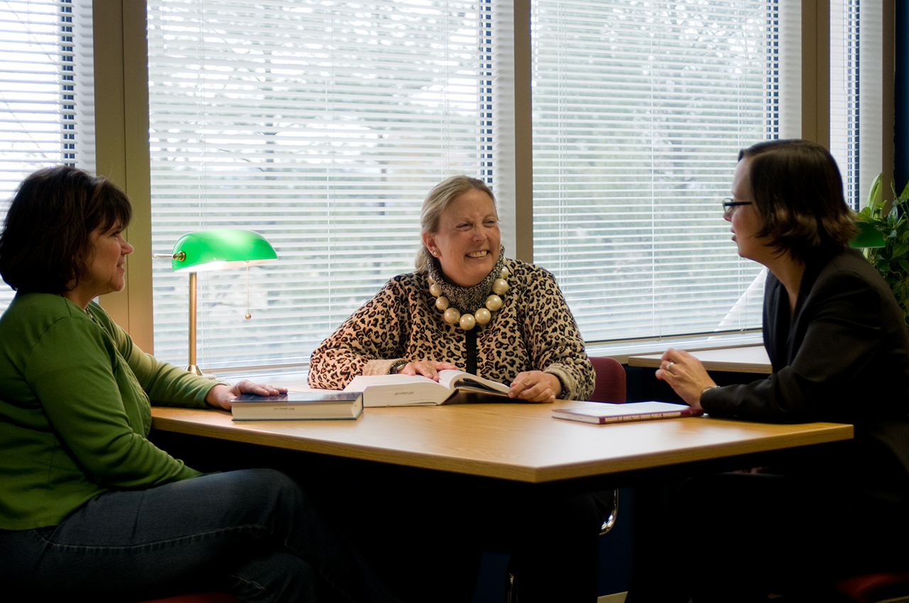 three women sitting at table in the library