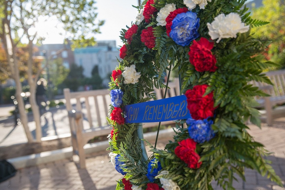 Memorial Day weath with red, blue, white flowers and words GW Remembers and a bench in the background